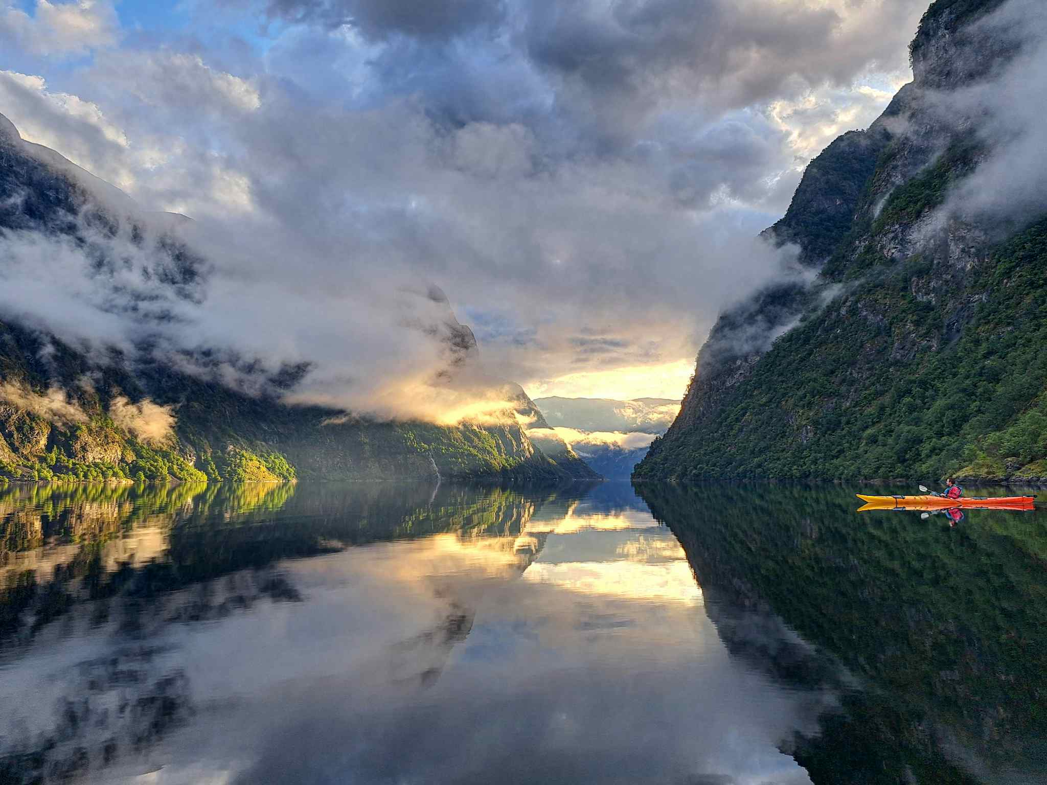 A calm, mirror-still Norwegian fjord with a kayaker